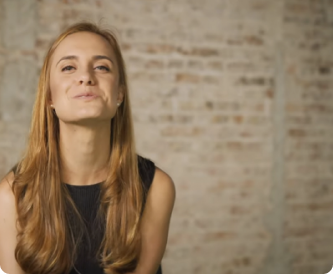 Mulher sentada sorrindo com uma sala com uma parede de tijolos ao fundo
